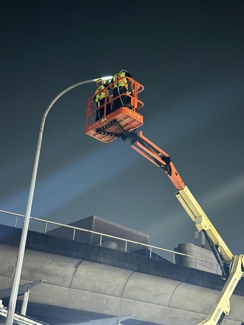 Two workers in a boom lift basket service a street light at night.